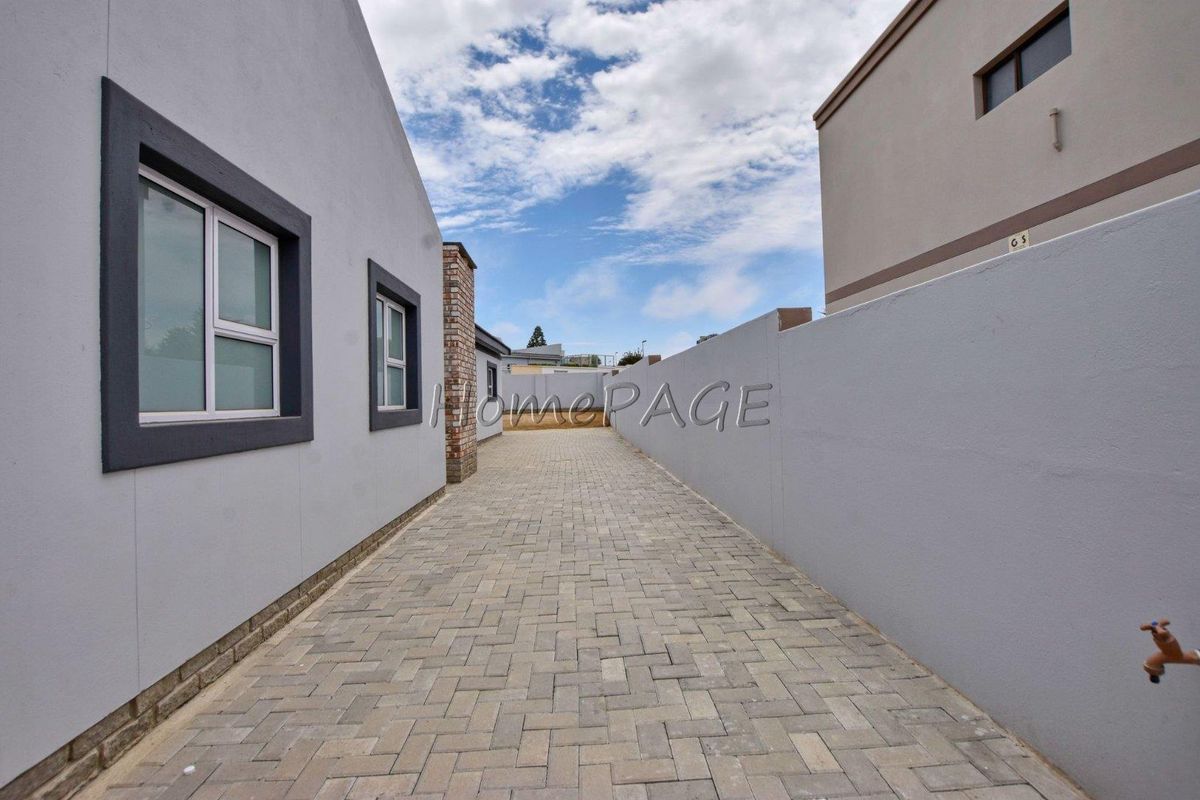 A paved side passage or driveway area between two residential structures, featuring a boundary wall and exterior water tap.