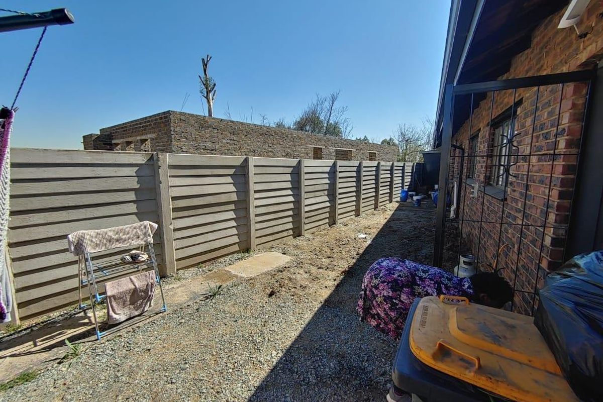 Rear exterior area featuring a precast concrete boundary wall, exposed brick house facade, and an unlandscaped gravel yard.