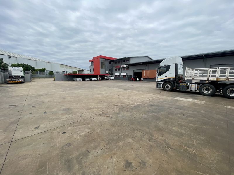 Spacious industrial yard featuring a large concrete surface, warehouse facility, and covered parking area suitable for heavy vehicle access and logistics operations.