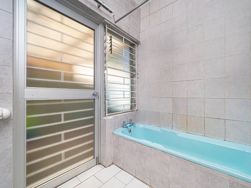 A dated bathroom featuring a built-in blue bathtub, tiled walls and flooring, and a frosted glass door with security bars.