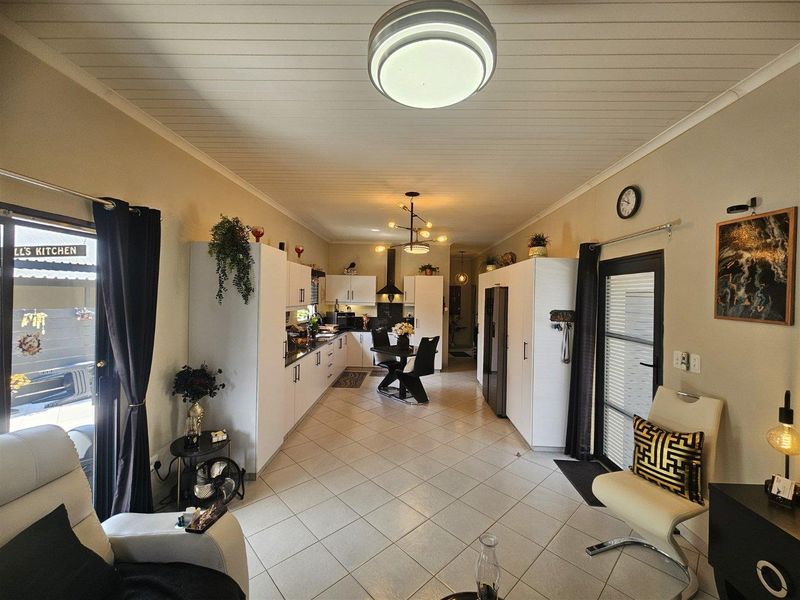 An open-plan kitchen and living area featuring white cabinetry, tiled flooring, and a tongue and groove ceiling with direct access to the exterior.