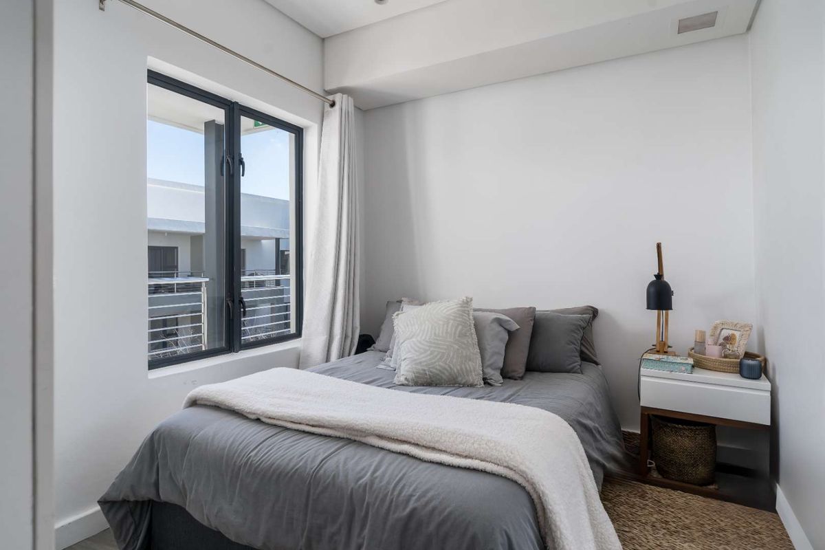 A bright and modern bedroom featuring large windows that provide natural light and a view of the surrounding apartment complex.