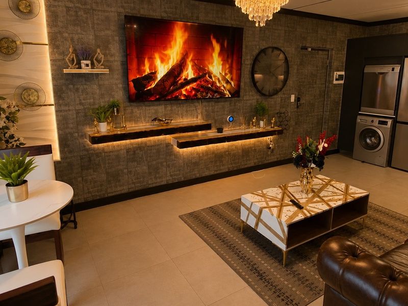 Modern open-plan living area featuring a textured feature wall with integrated floating shelves, recessed lighting, and a convenient laundry nook with built-in appliances.