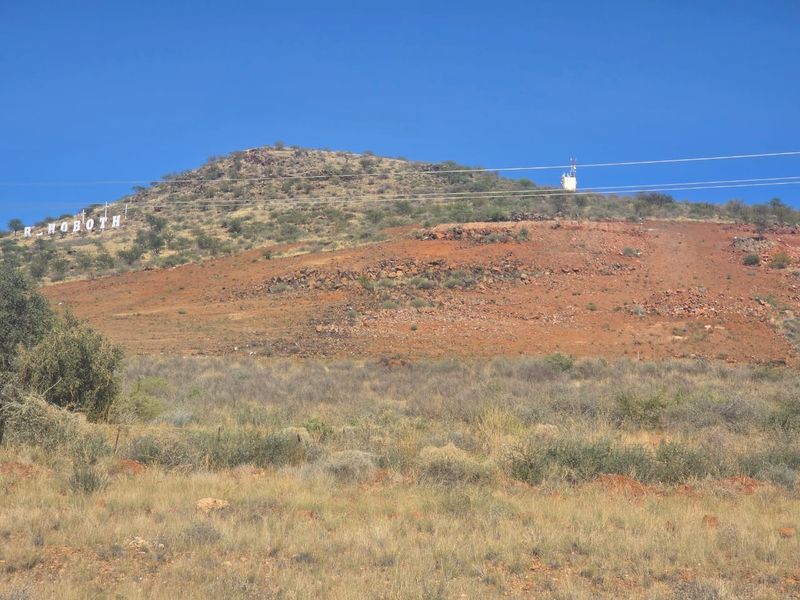 A scenic view of a rugged hillside landscape featuring natural vegetation, overhead power lines, and a distant telecommunications tower.