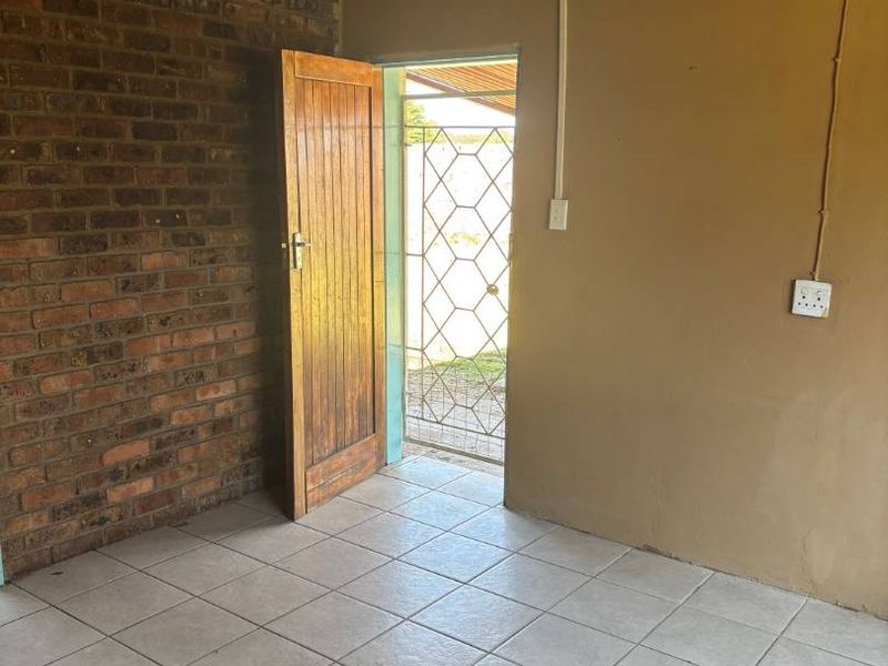 An empty entry area featuring exposed brickwork, a timber ceiling, and tiled flooring, leading to an exterior security gate.