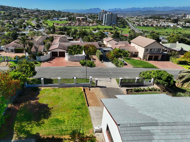 Aerial view of the property showing the driveway, front garden, perimeter fencing, and surrounding suburban neighborhood landscape.