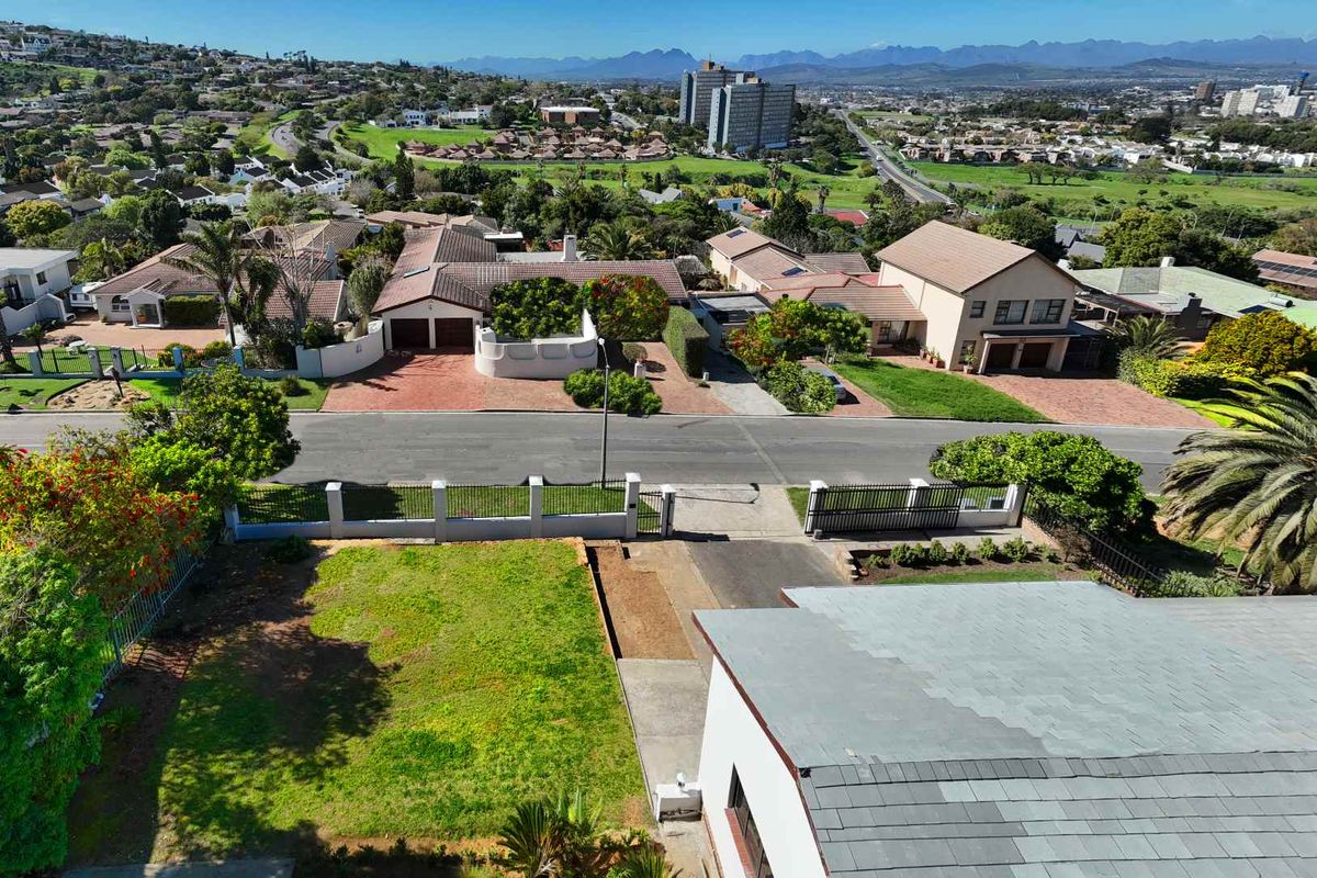 Aerial view of the property showing the driveway, front garden, perimeter fencing, and surrounding suburban neighborhood landscape.
