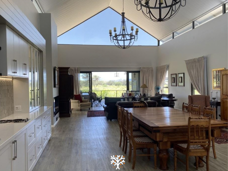 Spacious open-plan living area featuring a high vaulted ceiling, modern built-in kitchen cabinetry, a fireplace, and large sliding doors opening to a scenic view.