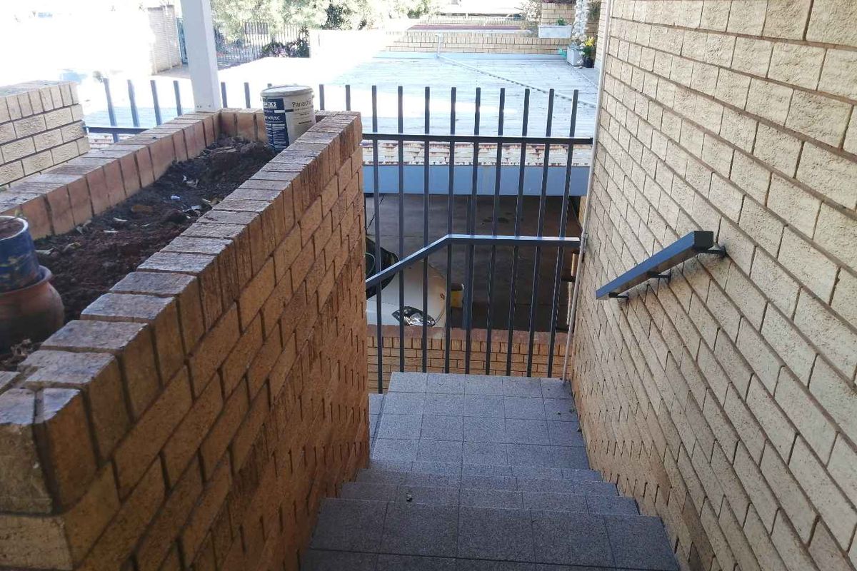 Exterior staircase with brick retaining wall and metal handrail leading down to a lower level area.