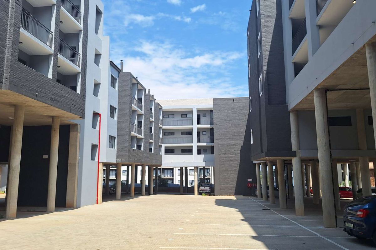 View of the apartment complex exterior featuring a paved parking area, concrete support columns, and multi-level residential balconies.