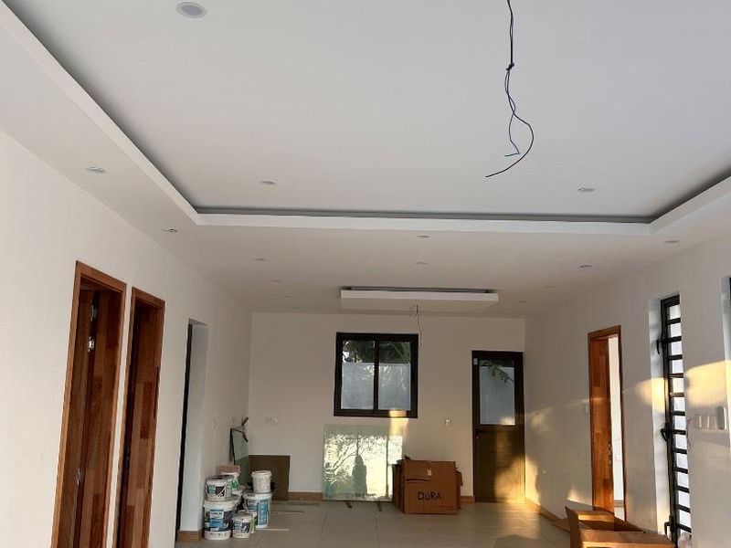 A spacious, light-filled open-plan living area featuring neutral tiled flooring, recessed ceiling lighting, and timber door frames, currently in a finishing stage.