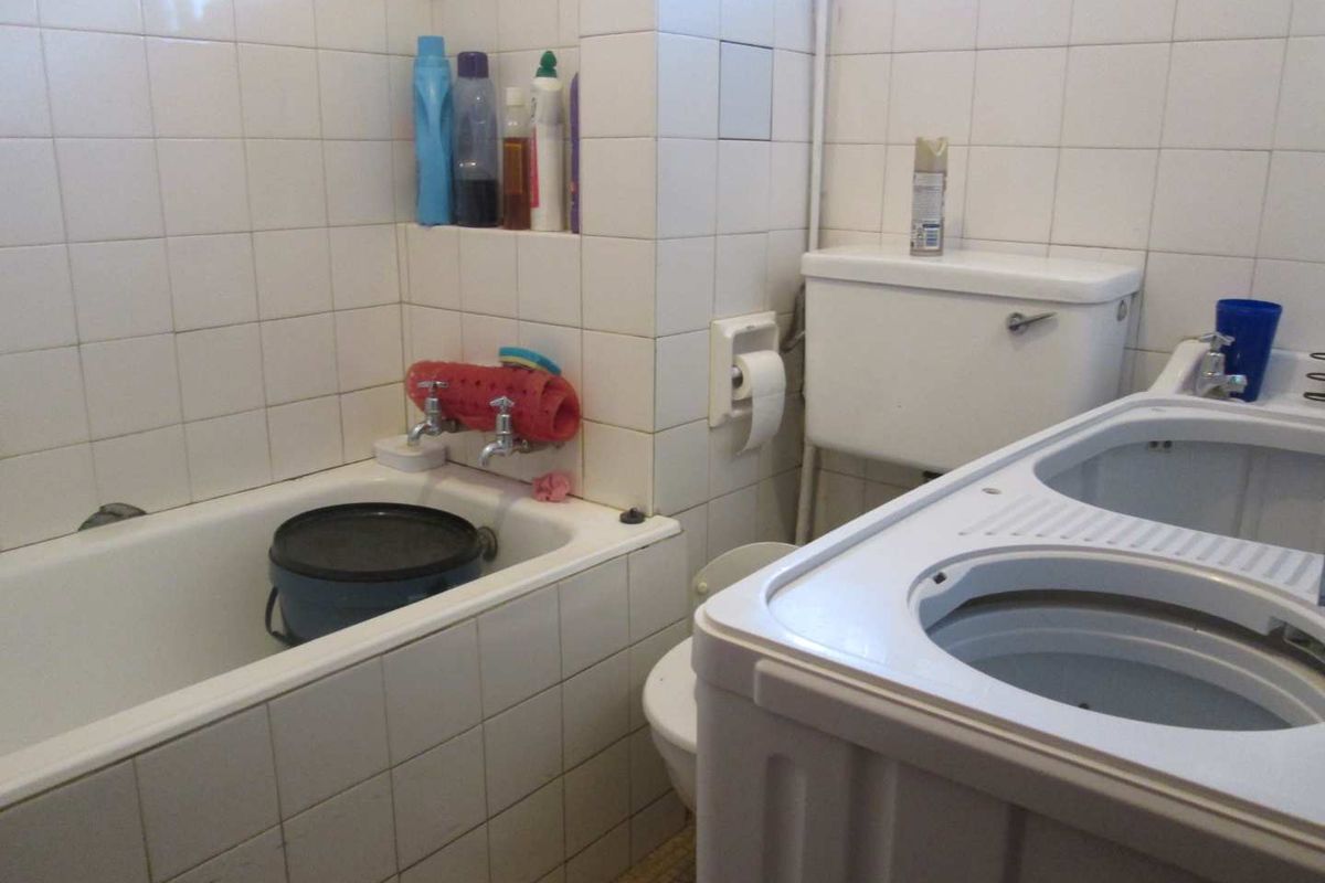 A dated bathroom featuring a built-in bathtub, ceramic wall tiling, and a standard toilet cistern, requiring modernization of finishes and fixtures.