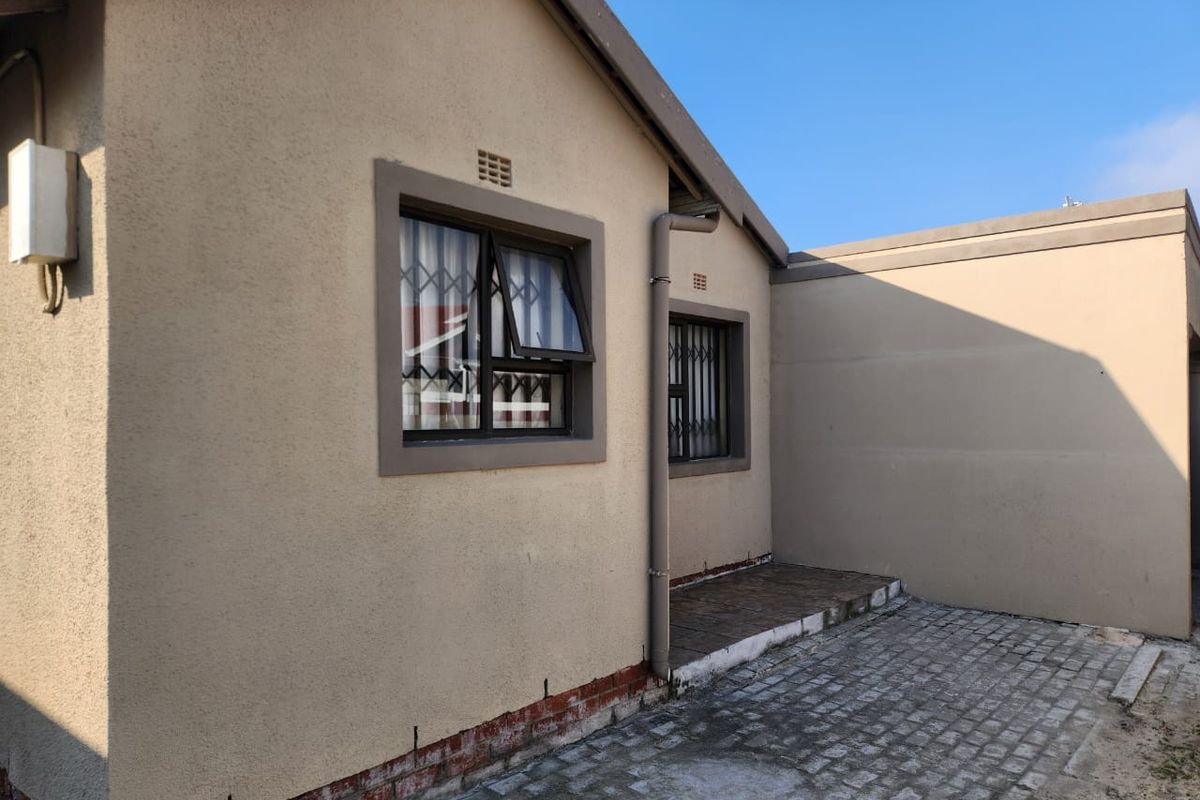 Rear exterior view of the property featuring plastered walls, security-fitted windows, a paved courtyard area, and functional drainage downpipes.