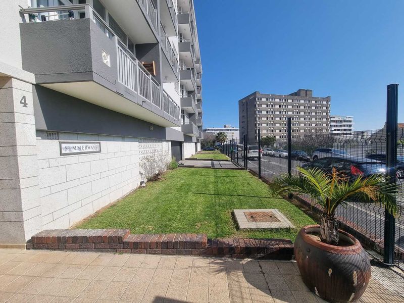 Front exterior view of the Summerways apartment building featuring a manicured lawn, paved walkway, and secure perimeter fencing.