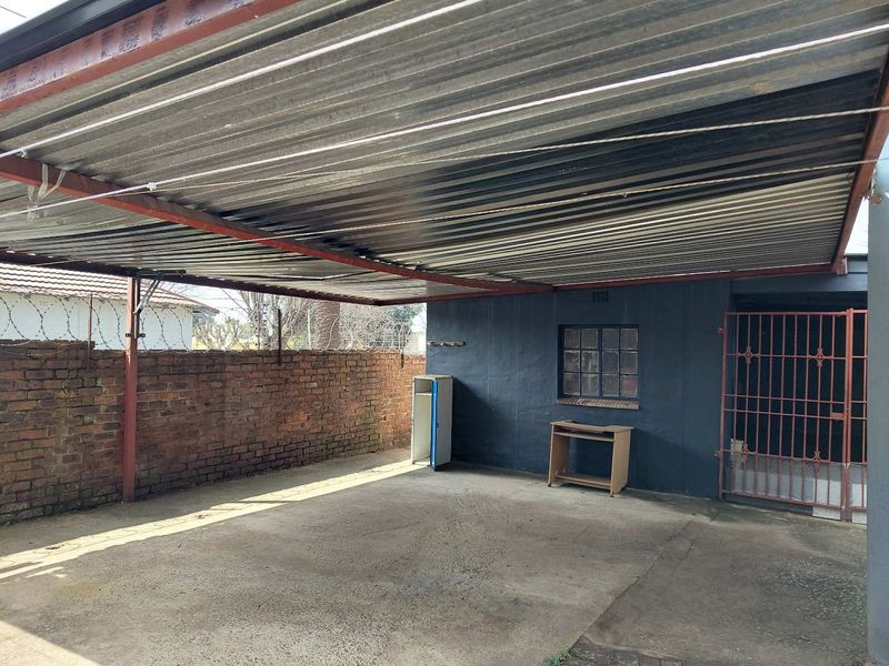 A covered outdoor parking area featuring a corrugated metal roof, concrete flooring, and secure perimeter brick walling with razor wire.