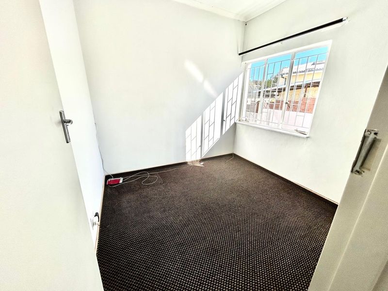 A vacant bedroom featuring carpeted flooring and a window fitted with security bars.