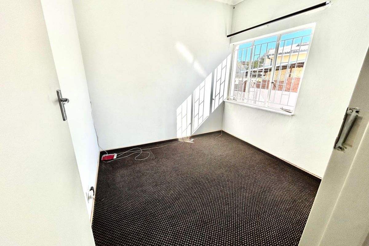 A vacant bedroom featuring carpeted flooring and a window fitted with security bars.