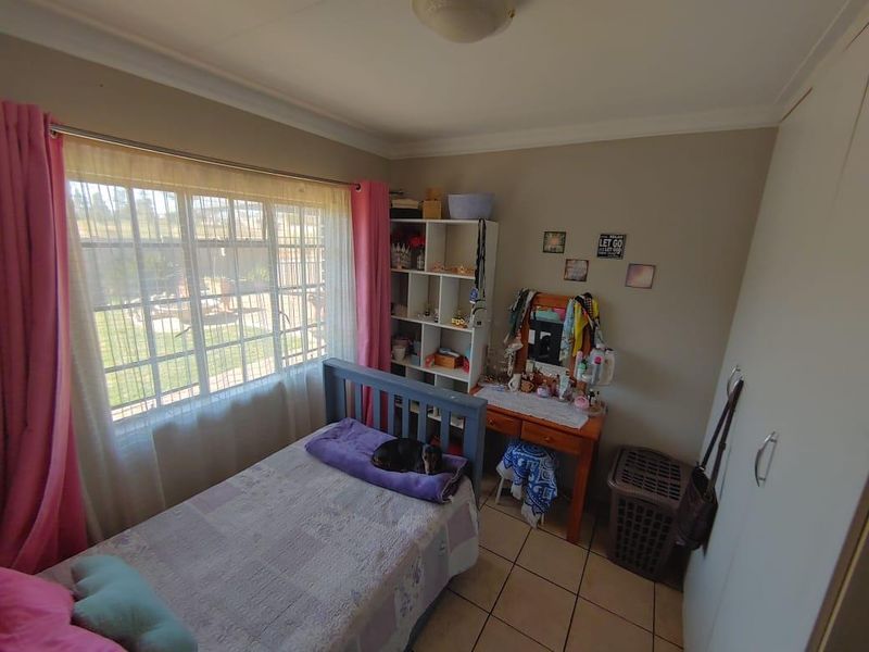 A functional bedroom featuring tiled flooring, a built-in wardrobe, and a large window with security bars, offering a bright and practical living space.