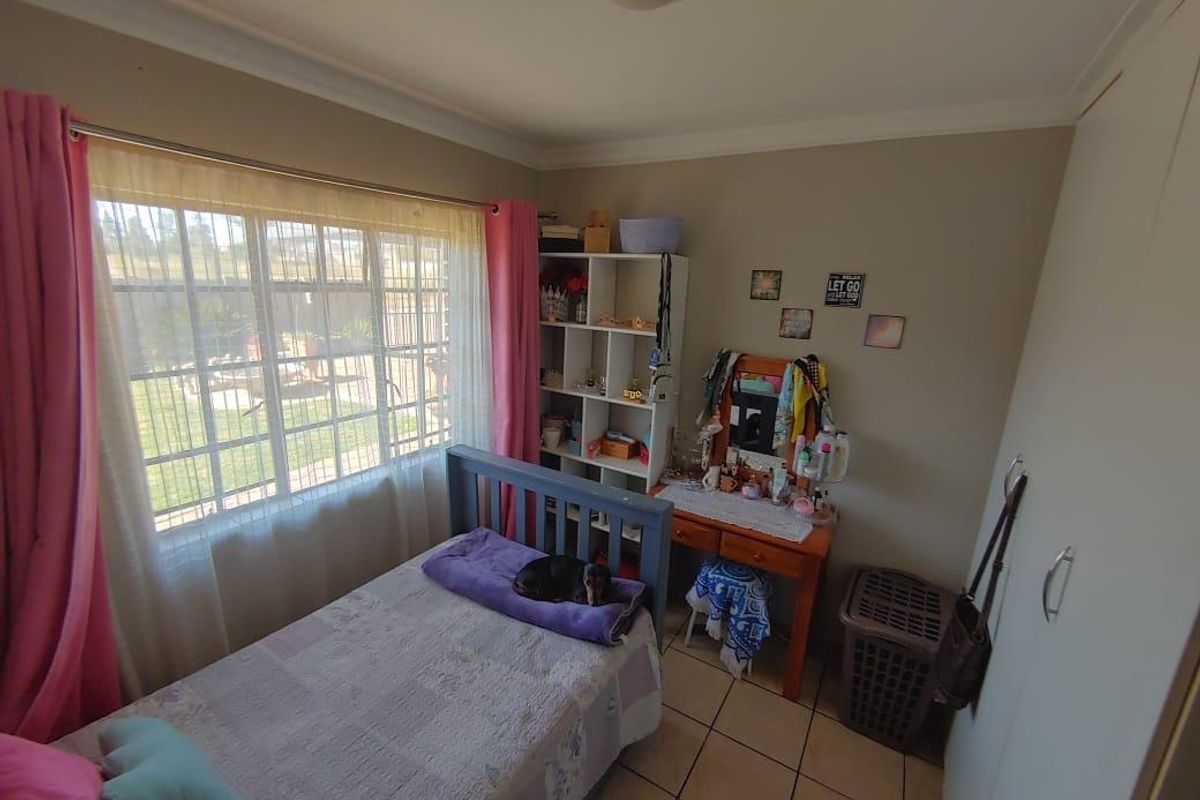 A functional bedroom featuring tiled flooring, a built-in wardrobe, and a large window with security bars, offering a bright and practical living space.