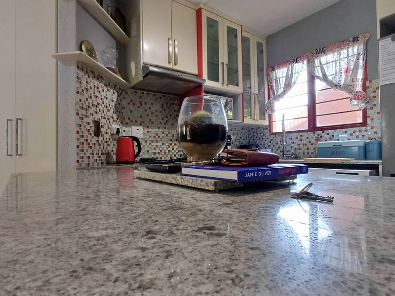 A functional kitchen featuring granite countertops, mosaic tile backsplash, and ample built-in cabinetry with glass-front display units.