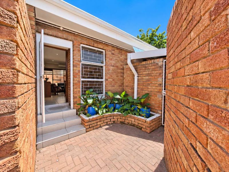 A private rear courtyard featuring brick paving, a built-in brick planter box, and direct access to the interior living space via tiled steps.