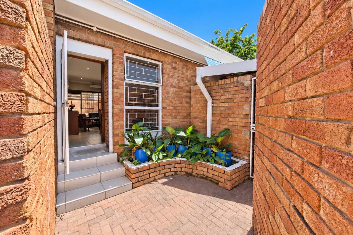 A private rear courtyard featuring brick paving, a built-in brick planter box, and direct access to the interior living space via tiled steps.