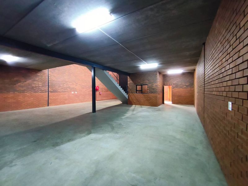 Spacious industrial utility area featuring exposed brick walls, concrete flooring, and a steel-supported staircase, suitable for storage or workshop use.