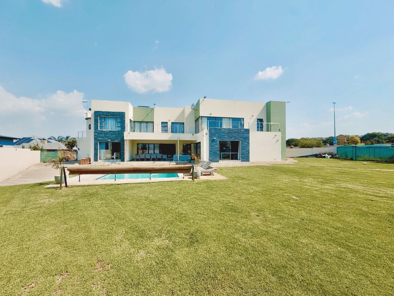 Rear view of a modern two-story house featuring stone cladding accents, a swimming pool, and a spacious lawn.