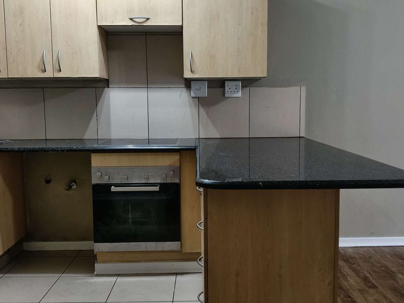 A functional kitchen featuring light wood cabinetry, granite countertops, a built-in oven, and a tiled backsplash, currently awaiting appliance installation.