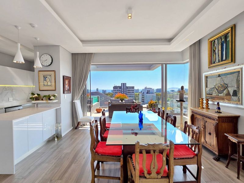 Spacious open-plan dining and kitchen area featuring modern cabinetry, recessed ceiling lighting, and seamless access to a balcony with expansive city and sea views.