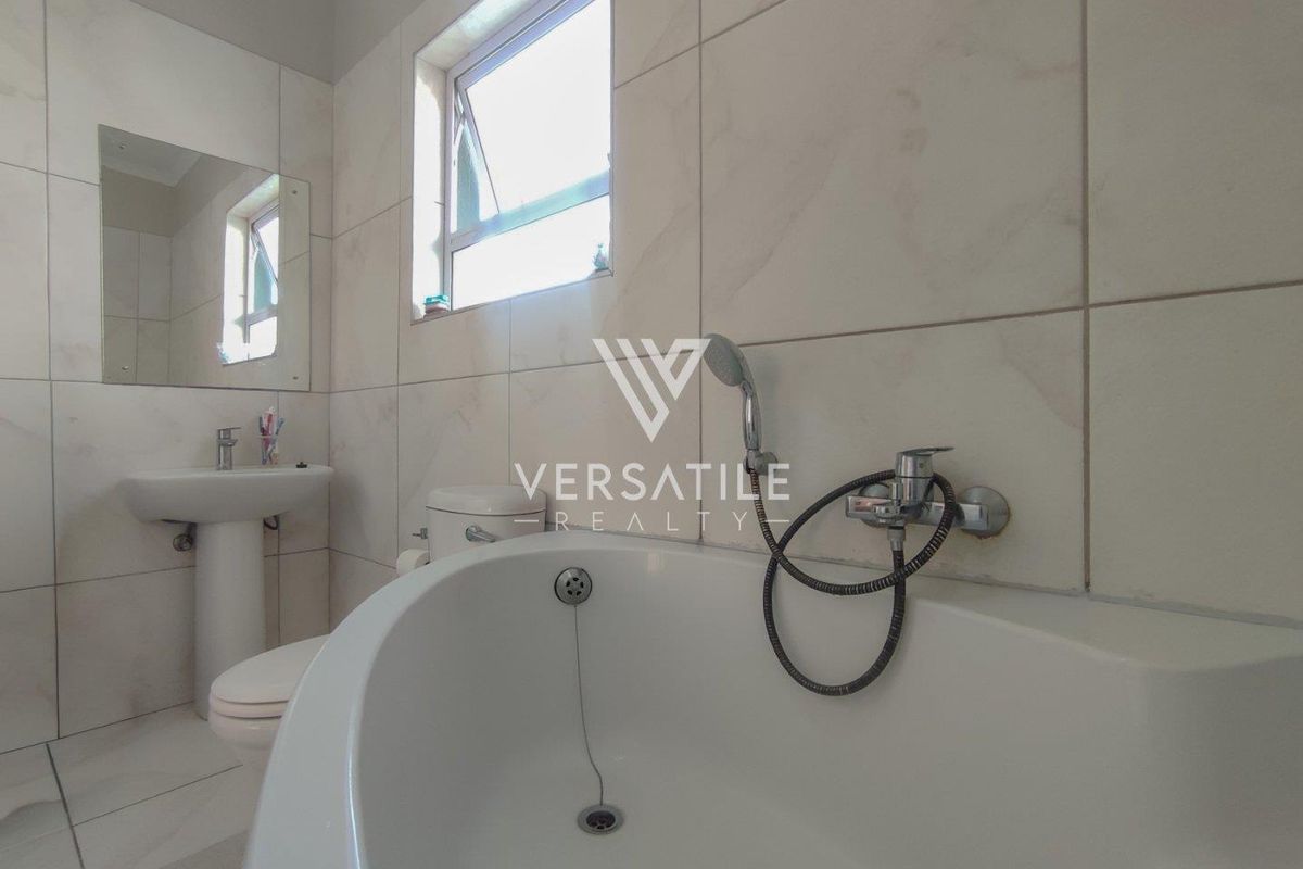 A clean, modern bathroom featuring floor-to-ceiling light-toned tiling, a pedestal basin, a toilet, and a bathtub with a handheld shower fixture.