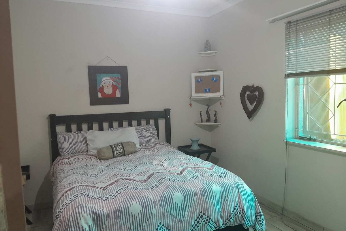 A standard bedroom featuring tiled flooring, a window with security bars, and venetian blinds.