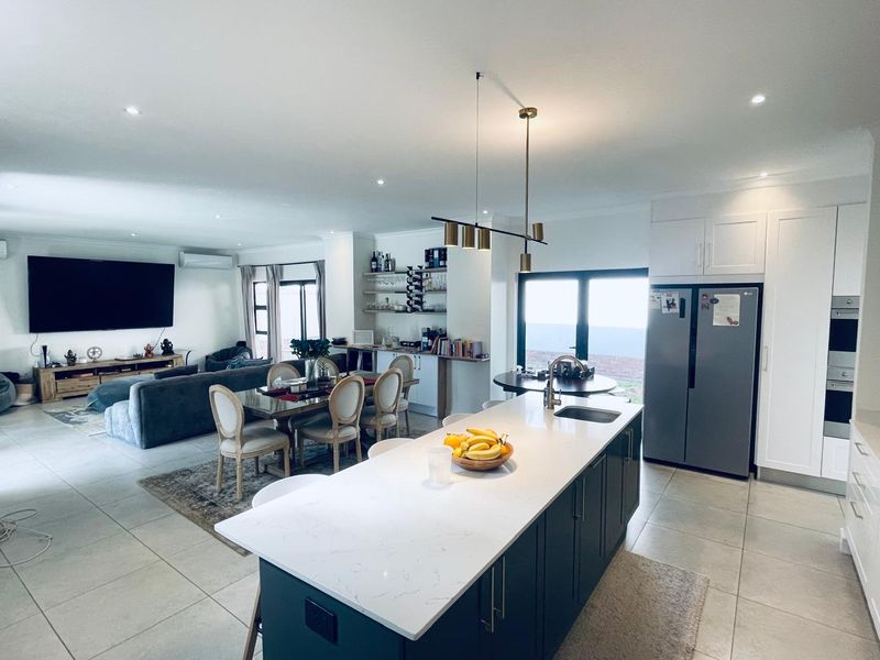 Spacious open-plan living area featuring a modern kitchen with a central island, quartz countertops, and integrated appliances, flowing into the dining and lounge space.