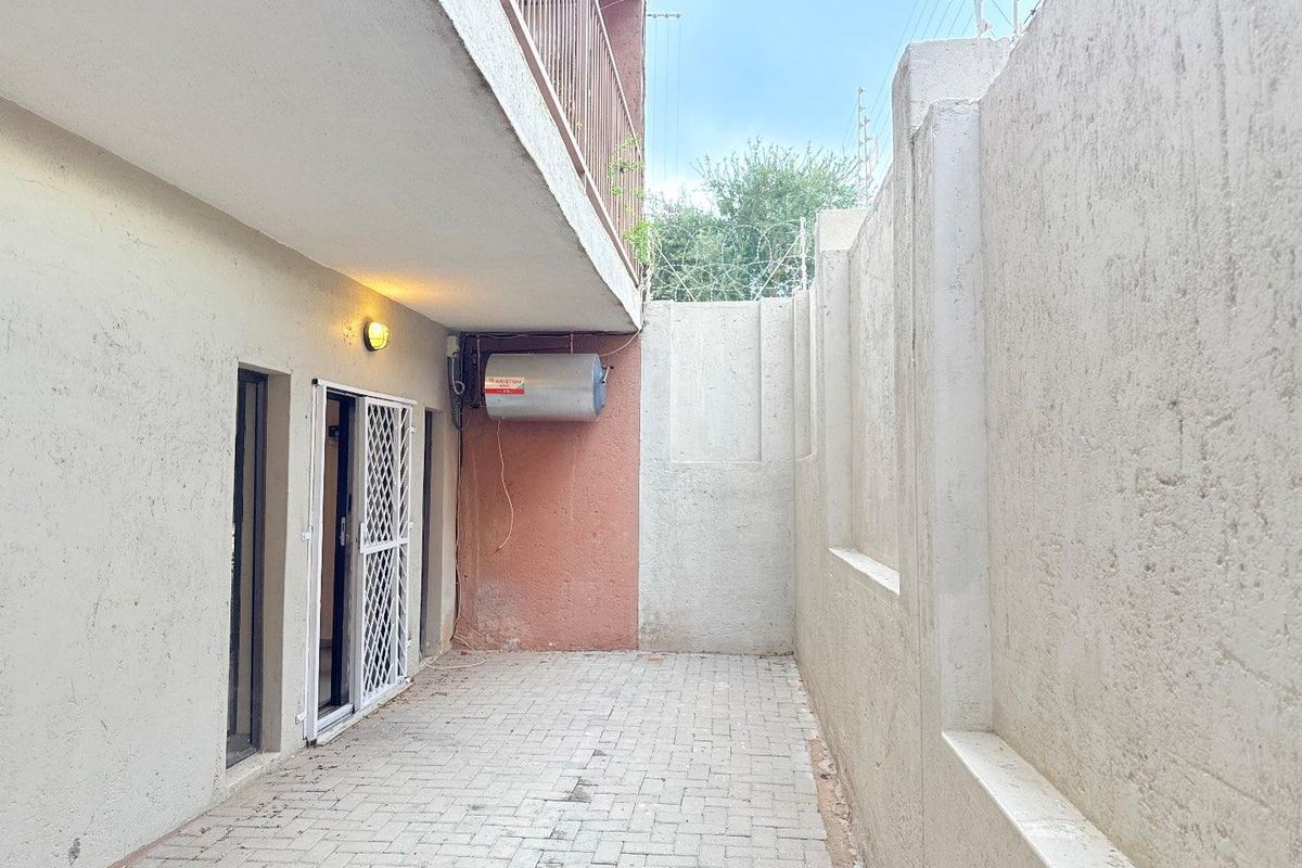 A private paved courtyard area featuring a wall-mounted electric water heater, security gate access, and high perimeter walls with security fencing.