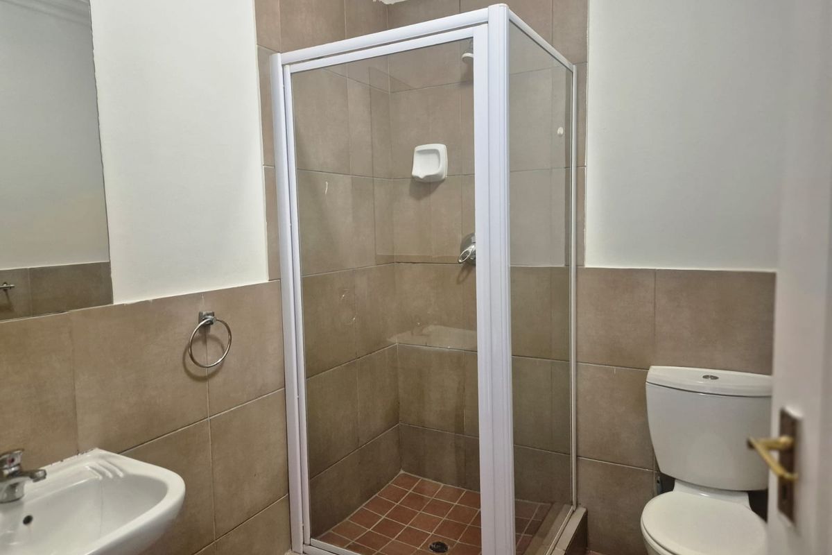 A functional bathroom featuring a shower enclosure, wall-mounted basin, and toilet with neutral wall tiling.
