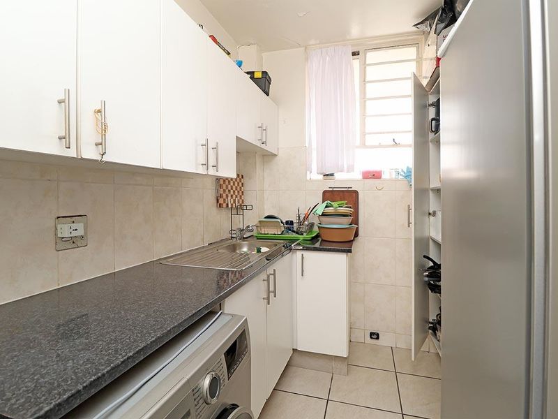 Compact scullery featuring white cabinetry, granite countertops, a stainless steel sink, and tiled finishes, providing functional utility space.