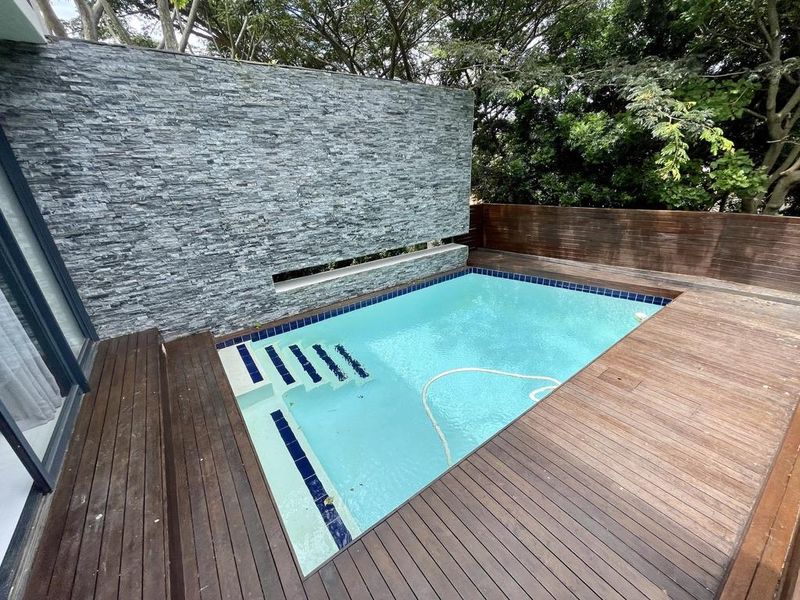 A well-maintained outdoor pool area featuring a modern stone feature wall, timber decking, and surrounding privacy fencing.