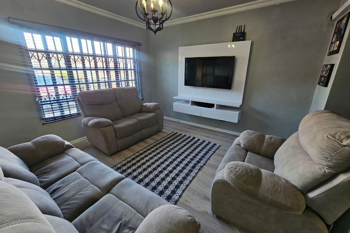 A comfortable living room featuring a built-in media console, laminate flooring, crown molding, and security bars on the window.
