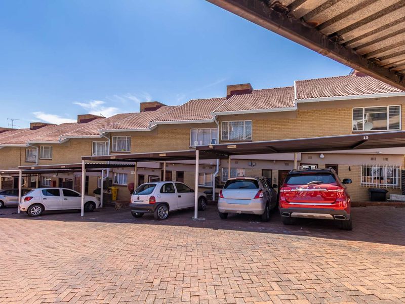 Front exterior view of a multi-unit apartment complex featuring brick facades, tiled roofing, and covered carport parking spaces on a paved driveway.