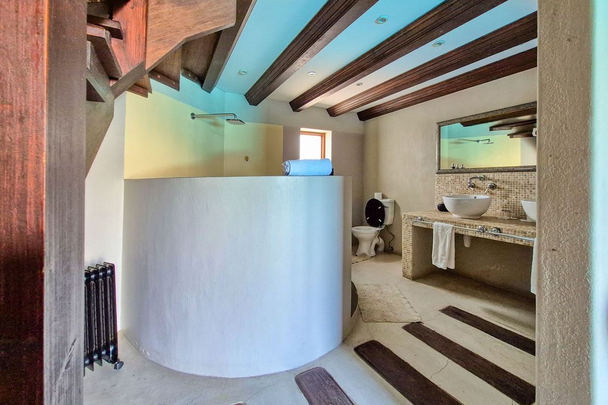 Unique bathroom featuring exposed timber ceiling beams, a curved shower partition, and a built-in mosaic-tiled vanity with dual vessel sinks.