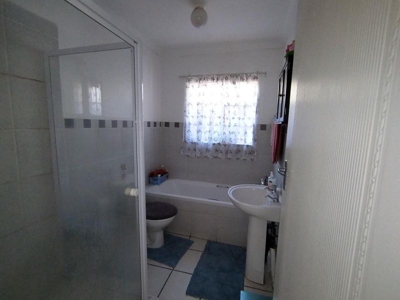 A functional bathroom featuring a shower enclosure, bathtub, pedestal basin, and toilet with tiled finishes.
