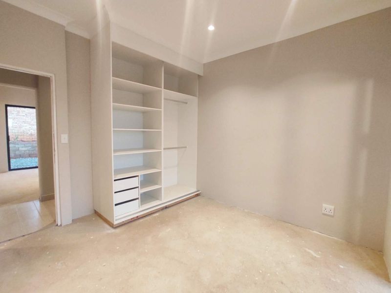An empty bedroom featuring a built-in wardrobe with shelving and hanging space, neutral wall paint, and unfinished flooring awaiting final installation.