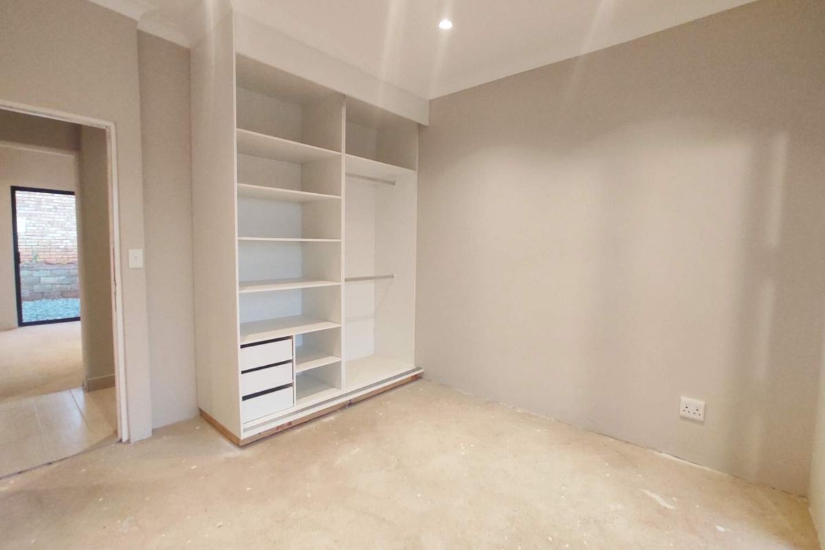 An empty bedroom featuring a built-in wardrobe with shelving and hanging space, neutral wall paint, and unfinished flooring awaiting final installation.