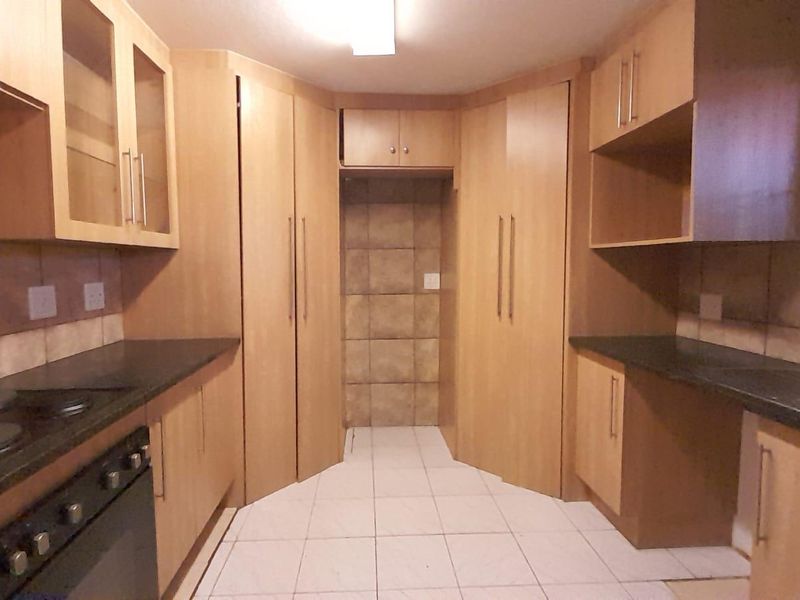 A functional kitchen featuring light wood cabinetry, dark laminate countertops, built-in oven and hob, and tiled flooring with a dedicated space for a refrigerator.