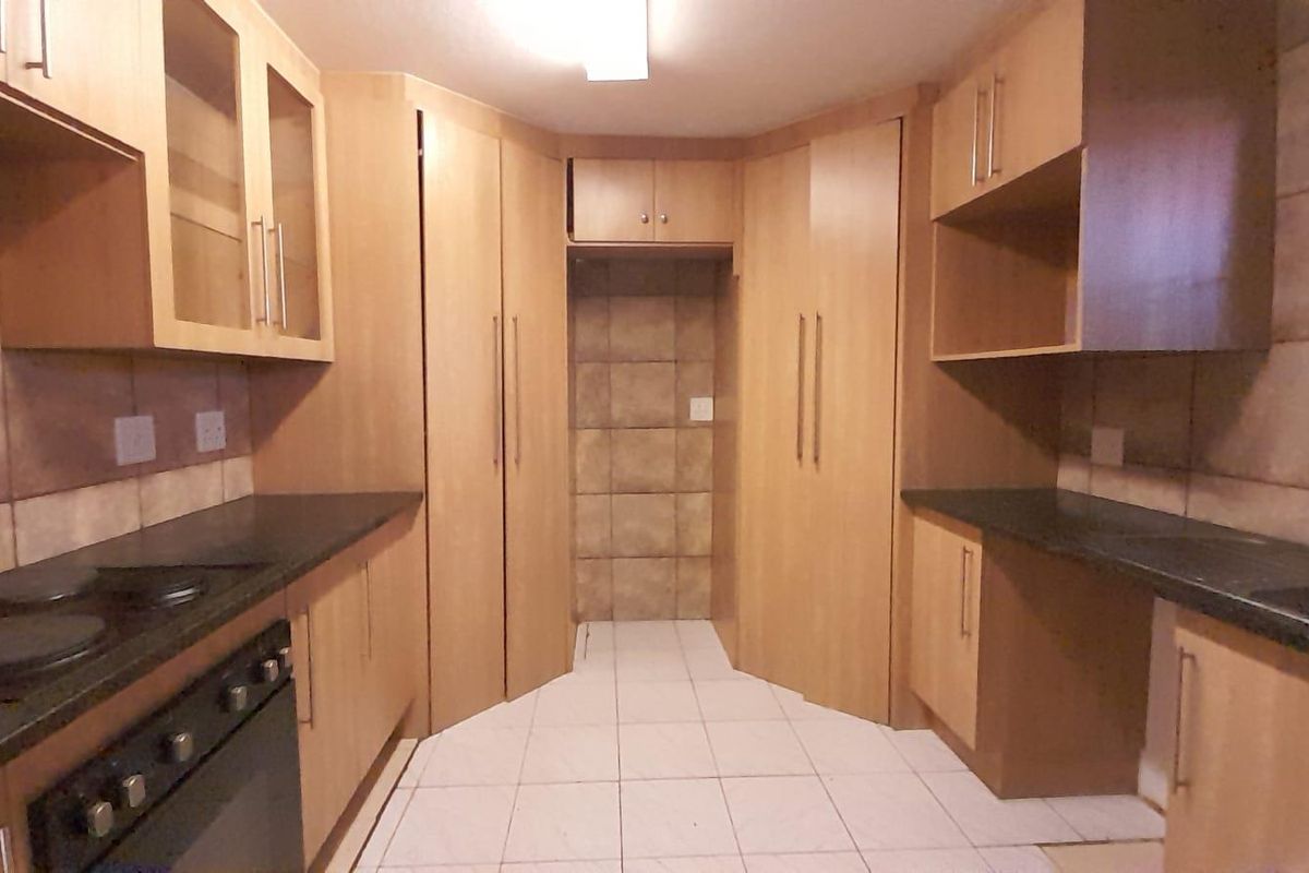 A functional kitchen featuring light wood cabinetry, dark laminate countertops, built-in oven and hob, and tiled flooring with a dedicated space for a refrigerator.