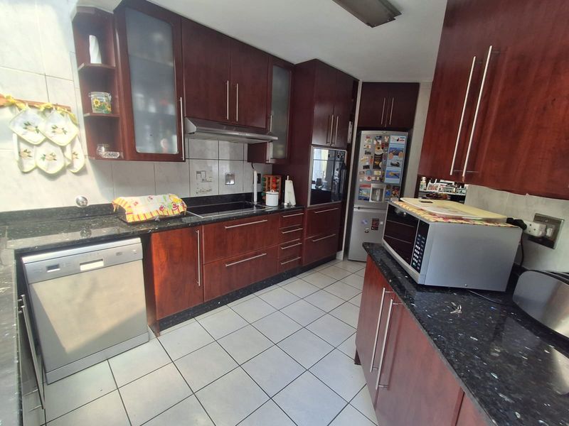 A functional kitchen featuring dark wood cabinetry, granite countertops, built-in oven, and ceramic hob with tiled flooring and backsplash.