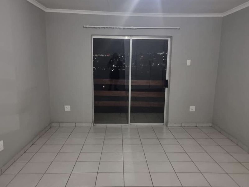 An empty living room featuring neutral grey walls, tiled flooring, and a sliding glass door providing access to an outdoor balcony area.