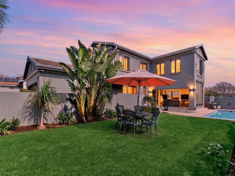 A well-maintained rear garden featuring a swimming pool, paved patio area, and modern double-story house facade with large sliding doors.