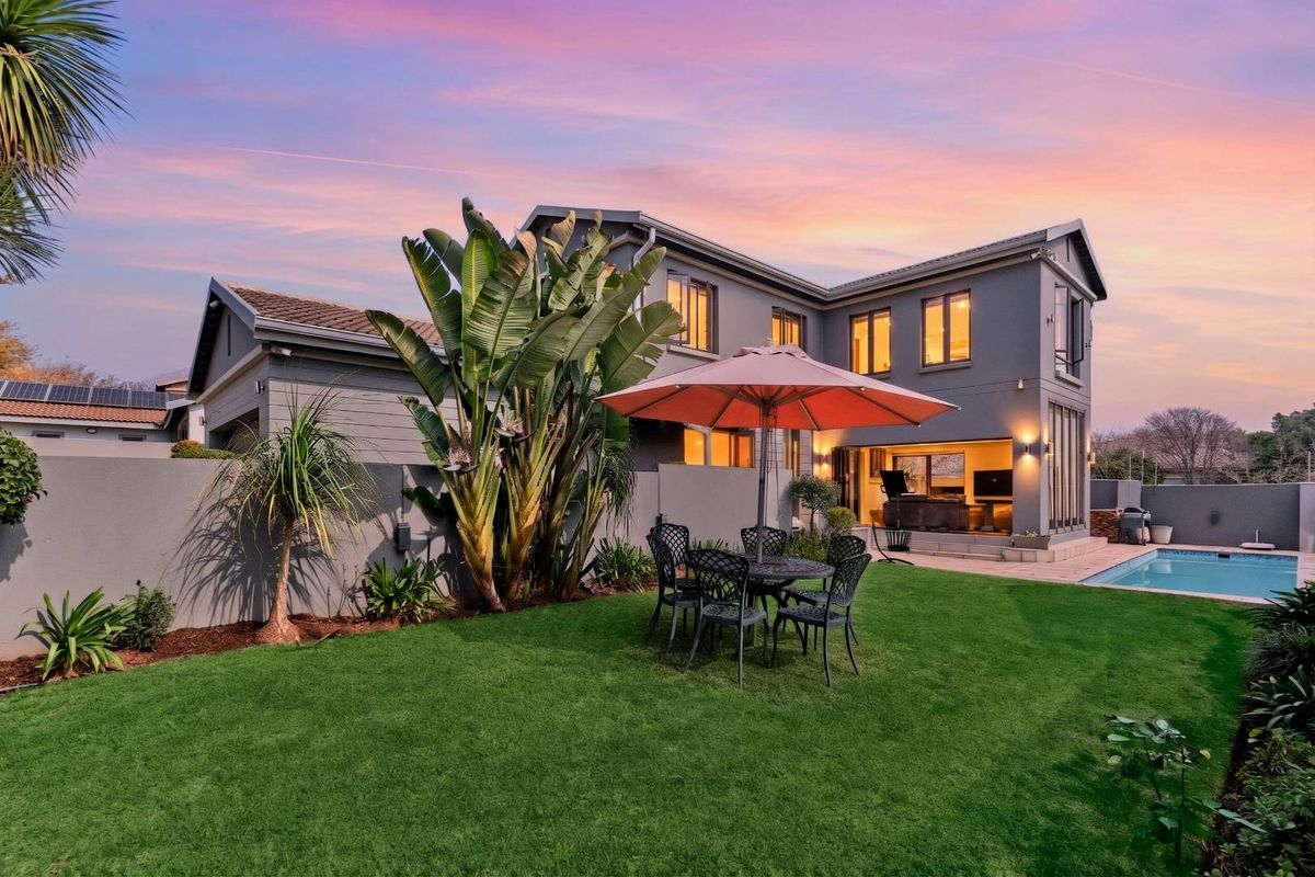 A well-maintained rear garden featuring a swimming pool, paved patio area, and modern double-story house facade with large sliding doors.
