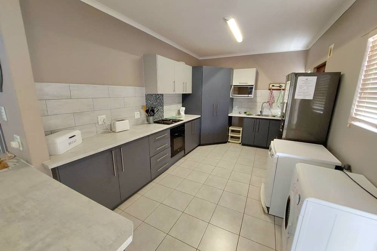 A functional kitchen featuring grey cabinetry, tiled splashbacks, built-in oven and hob, and integrated laundry space with tiled flooring.